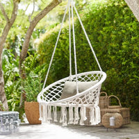 Chaise Suspendue de Style Bohème avec Pompons dans un jardin avec des plantes et des buissons