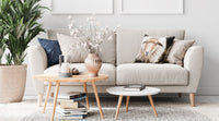 Un canapé avec une housse beige dans un salon, devant il y deux petites table basses rondes et sur le côté une plante.