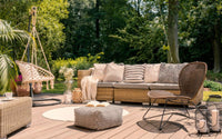 Salon de jardin extérieur sur une terrasse, avec une chaise suspendue, un canapé , un pouf de sol, une chaise scandinave, des bougies et un tapis.