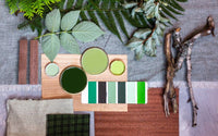 Photo prise d'en haut pour mettre en valeur la palette de couleur vert et marron avec des couvercle de pot de peinture, un nuancier de vert, des feuilles de différentes plantes vertes, des bouts de bois, des carrés tissus et de papiers.