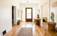 Entrée intérieure en longueur, avec des mur blanc et du parquet au sol, la porte d'entrée est vitrée, un porte manteau sur la gauche et une console sur la droite.