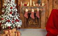 Sapin blanchi, décoré de boules rouges, avec des cadeaux au pied, à côté d'une cheminée où se trouve des chaussettes de Noël, et des bougies posées.