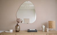 Mur rose-beige pastel, sur lequel est accroché un miroir bulle, en dessus un meuble en bois sur lequel est posé de la décoration.