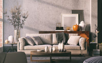 Photo d'un salon : un canapé avec des coussins et un plaid. derrière un meuble avec des cadres et des vases décoratifs posés. devant une table basse ronde en bois avec de la décoration posée dessus.
