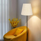 Abat Jour Lampadaire Simple et Moderne en Tissu et Fer sur fond beige avec des fleurs et un fauteuil