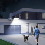 Éclairage Extérieur Solaire LED avec Capteur de Mouvement et Télécommande au desuss d'un garage éclairant un homme avec son chien