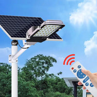 Éclairage Extérieur Solaire LED Étanche de Style Lampadaire avec Télécommande devant des arbres sur fond de ciel bleu avec une main tenant la télécommande