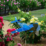 Girouette de Toit en Forme d'Avion en Métal sur fond d'un jardin avec des fleurs et de l'herbe