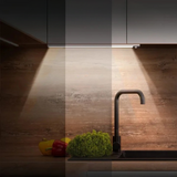Lampe Détecteur de Mouvement Rectangulaire pour Dessous de Meuble sous un meuble gris dans une cuisine au dessus d'un évier avec robinet noir
