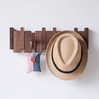 Porte Manteau Mural en Bois Massif avec 6 Crochets Pliables sur un mur gris tenant un chapeau de paille et un objet