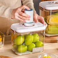 Rangement de Cuisine Style Boite Sous Vide sur une table avec des fruits à l'intérieur et une personne en train d'utiliser la pompe manuelle