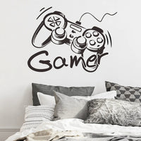 Sticker Mural Chambre en Forme de Manette avec Inscription Gamer collé sur un mur blanc avec un lit et des oreillers noir et blanc en dessous