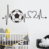 Sticker Mural Chambre Style Battement de Cœur avec un Ballon de Football collé sur un mur gris avec un berceau un coussin une peluche et des drapeaux devant et un fauteuil à droite avec un coussin