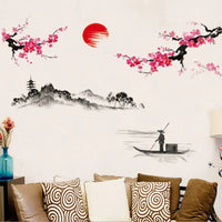 Sticker Mural Salon Lever de Soleil Style Japonais collé sur un mur blanc avec un canapé et des coussins en dessous et une table avec un pot de fleur sur la gauche